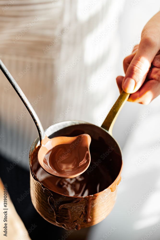 Beautiful young girl in beige apron is preparing delicious organic hot chocolate in old vintage ladle. Soft daylight, lifestyle photography, process of tasty drink creation. Close up Beautiful young girl in beige apron is preparing delicious organic hot chocolate in old vintage ladle. Soft daylight, lifestyle photography, process of tasty drink creation. Close up
