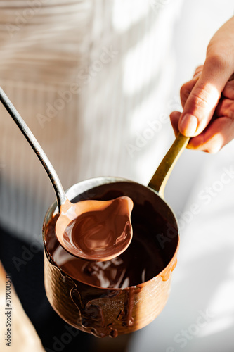 Beautiful young girl in beige apron is preparing delicious organic hot chocolate in old vintage ladle. Soft daylight  lifestyle photography  process of tasty drink creation. Close up