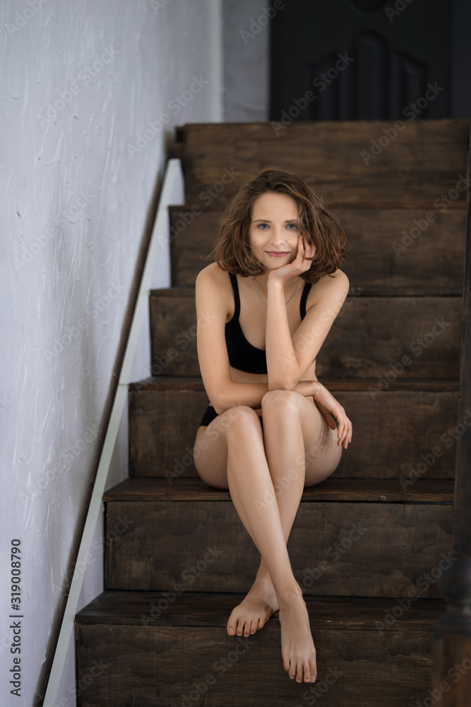 Beautiful girl in black bikini sitting on wooden stairs at home