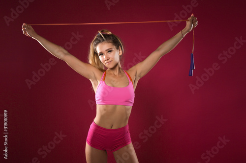 beautiful young woman in sportswear on a red background with a skipping rope in hands