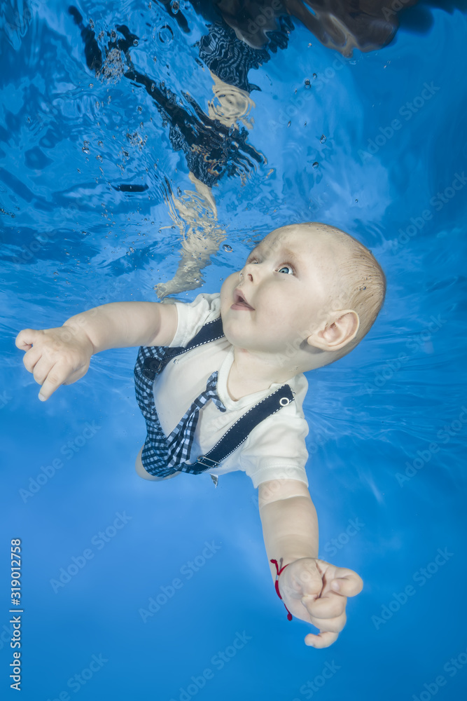 Little boy in a shirt and shorts with suspenders swims underwater. Healthy family lifestyle and children water sports activity. Child development, disease prevention
