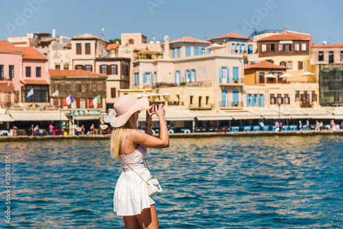Attractive female tourist/ influencer taking photo with a smartphone during sumer vacation.  Chania, Crete, Greece