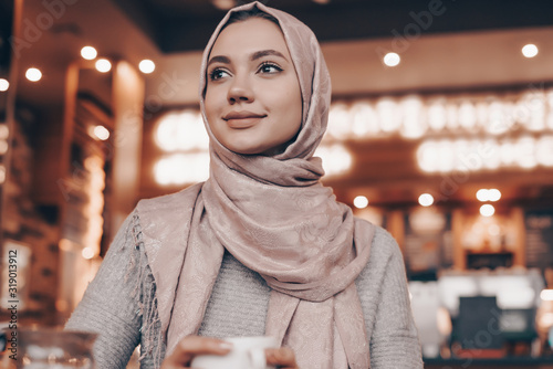 Muslim woman in a headscarf gently and hopefully looks and smiles in her hand a cup of tea