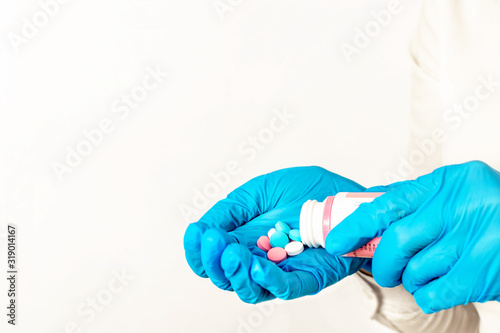 Close-up of hands in blue medical gloves holding a bottle with multi-colored pills. The doctor gives a dose of medication or vitamins and antibiotics to treat health in the palm of hand.