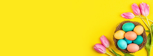 Stylish background with colorful easter eggs isolated on yellow background with pink tulip flowers. Flat lay, top view, mockup, overhead, template