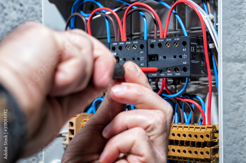 Electrician with screwdriver fixes the cable in a residential electrical distribution panel. Construction industry, electrical system. photo