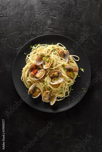 Seafood pasta. Clams in shells with spaghetti, dried tomatoes and lemon in black plate on black background copy space