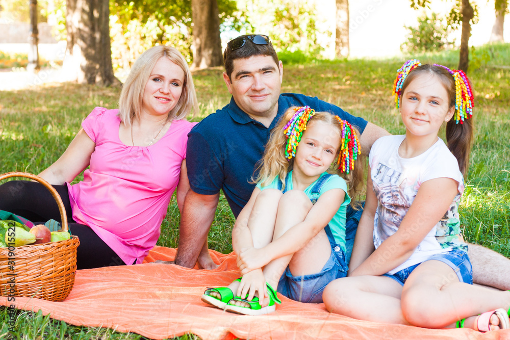 Happy Two Parent Family With Two Daughters On Orange Picnic Blanket In The Park
