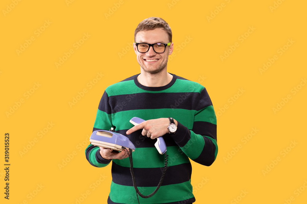Smiling young man talking on the phone. Man holds purple phone in his hands and calling on a yellow background. Studio photo. Smiling young man talking on the phone. Man holds purple phone in his hands and calling on a yellow background. Studio photo.