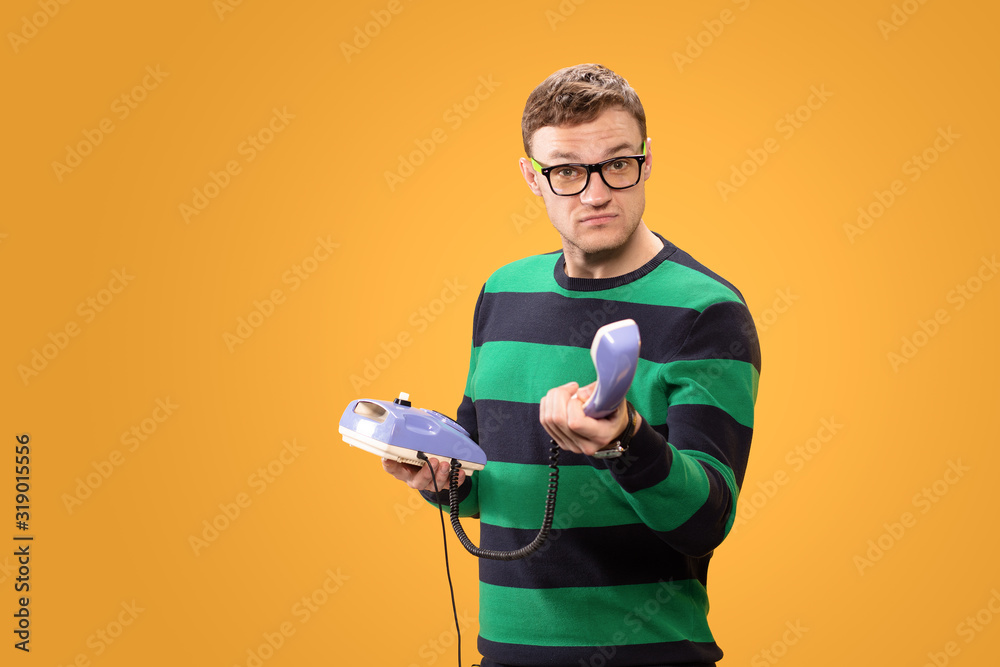 Handsome man aggressively offers to answer the call. Man holds purple phone in his hands and calling on a yellow background. Studio photo. Handsome man aggressively offers to answer the call. Man holds purple phone in his hands and calling on a yellow background. Studio photo.
