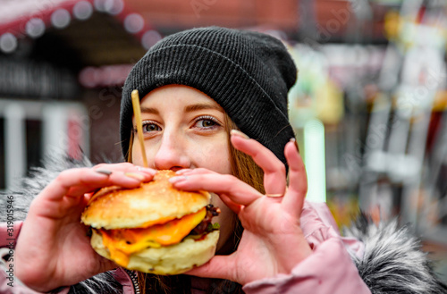 Street food. young woman holding juicy burger and eating oudoor winter