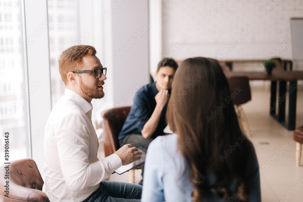 Confident businessman communicates with his subordinates on working issues. Manager listens attentively to his colleagues in modern office meeting against large window.Concept of office life. Confident businessman communicates with his subordinates on working issues. Manager listens attentively to his colleagues in modern office meeting against large window.Concept of office life.