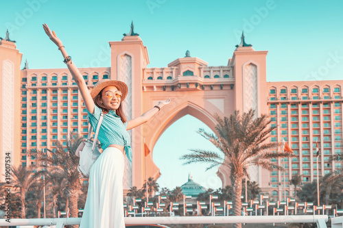 Happy asian girl traveller spreading her arms in front of the famous luxury Atlantis hotel building on a Jumeirah Palm Island in Duba, UAE photo