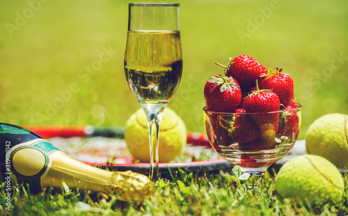 Tennis game. Strawberries, champagne and tennis balls with rackets on the green grass. Sport, recreation concept photo