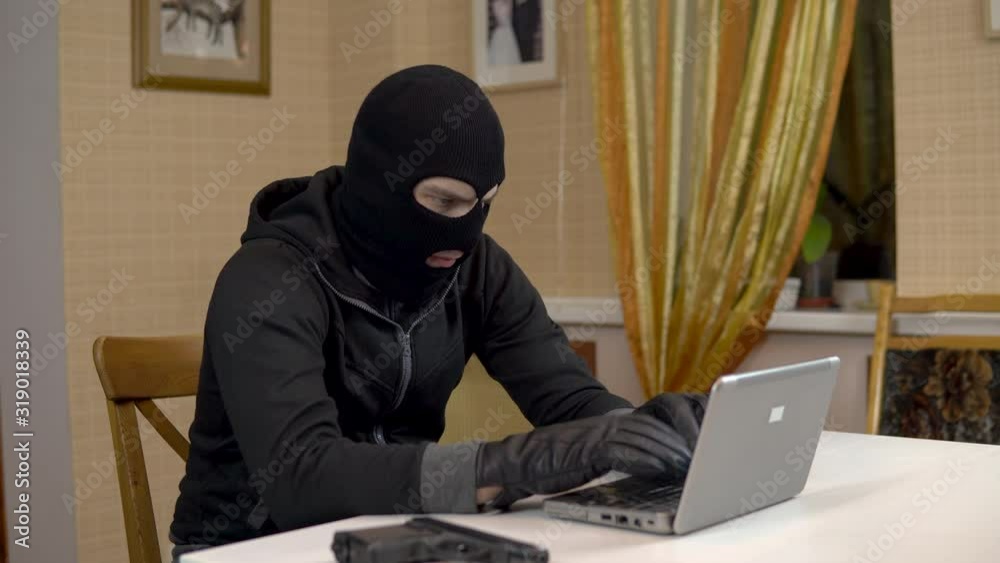A robber is trying to hack into a laptop. A masked thug is sitting in a house and cannot hack into a laptop. Theft of data from a computer. A robber is trying to hack into a laptop. A masked thug is sitting in a house and cannot hack into a laptop. Theft of data from a computer.