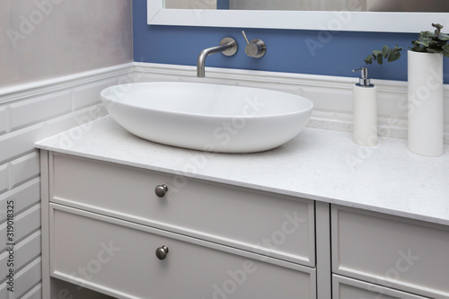 Bathroom interior in a blue pastel colors and a close up of a bathroom furniture. A bowl-shaped sink on a ultra thin quartzite countertop. Contemporary bathroom design. 