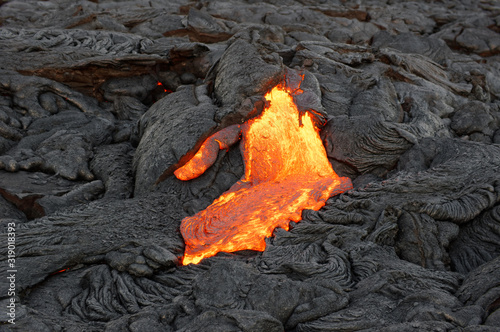 Hot magma of a lava flow from an active volcanic eruption emerges from a fissure and flows over previously deposited dark strongly structured rock, it cools slowly and solidifies - Hawaii, Kilauea