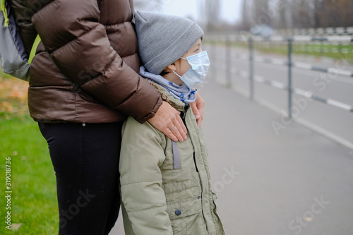 The kid is standing near mom in a medical mask. Protection against Chinese coronavirus. European tourists mom with a boy walk on the outskirts of Hong Kong.