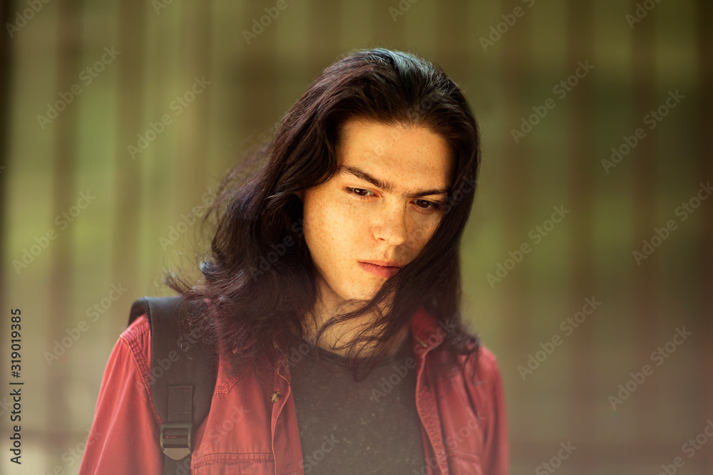 a young, handsome man with long hair and brown eyes walks down the street in a bright shirt and black jeans a young, handsome man with long hair and brown eyes walks down the street in a bright shirt and black jeans