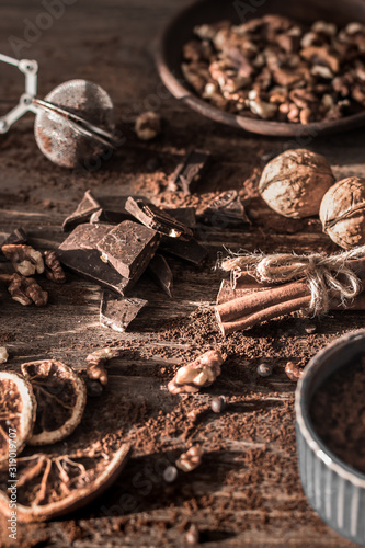 Ingredients for making hot chocolate. Walnuts, cocoa powder, cinnamon sticks and pieces of dark chocolate on a wooden background.