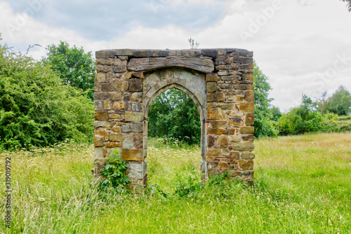 Canvas Print Ruined stone archway in grassy field