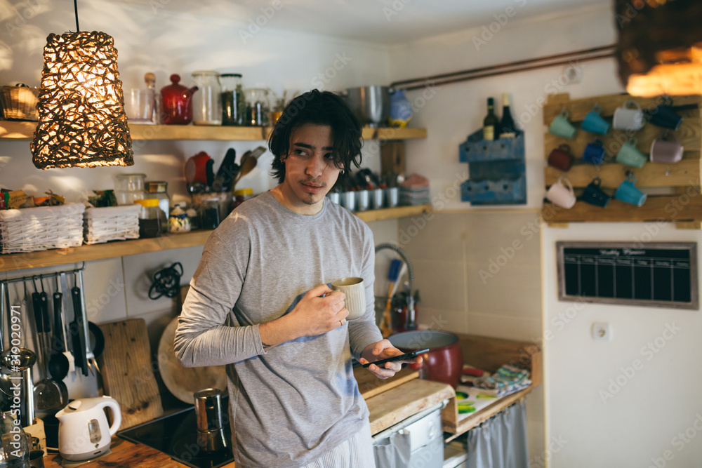 Fototapeta premium man drinking coffee using mobile phone in kitchen