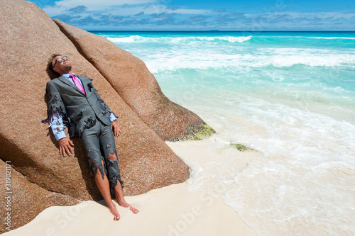Survivor castaway businessman washed up on a tropical beach in a ragged torn suit