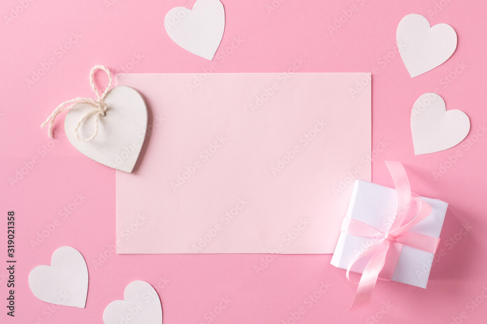 Gift with ribbon, white wooden hearts, pink paper and paper hearts on pink background. Flat lay, top view. Valentine day concept.