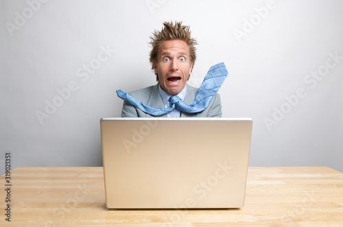 Surprised businessman freaking out in front of his computer while sitting at his desk 