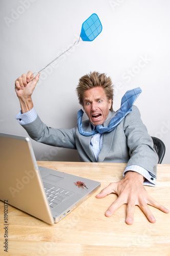 Frightened businessman swatting a bug crawling on his laptop computer