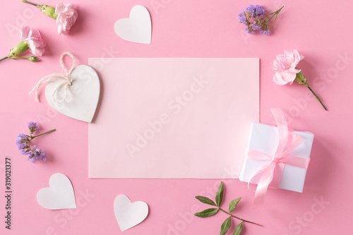 Gift with ribbon, white wooden hearts, flowers, pink paper and paper hearts on pink background. Flat lay, top view. Valentine day concept.