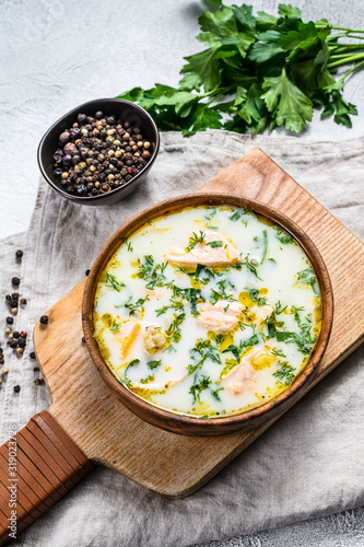 Creamy fish soup with salmon, trout, potatoes and parsley. Gray background, top view.