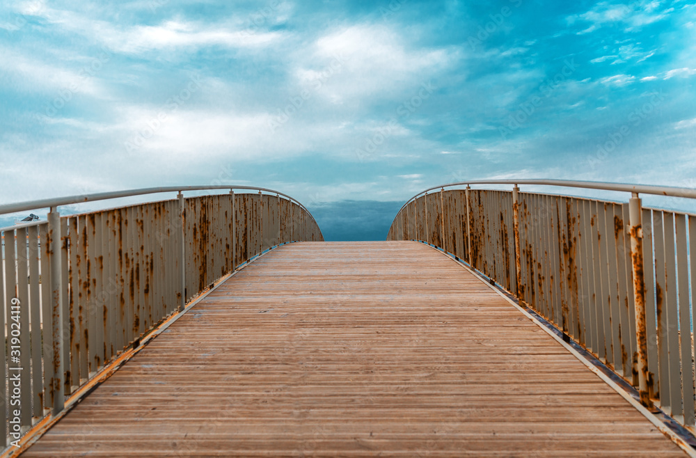 Wooden walking bridge with metal railing against the blue sky in perspective. Background with wood texture