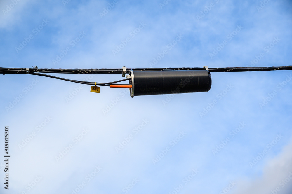 Overhead phone lines and splice canister, against a blue sky with white clouds Overhead phone lines and splice canister, against a blue sky with white clouds