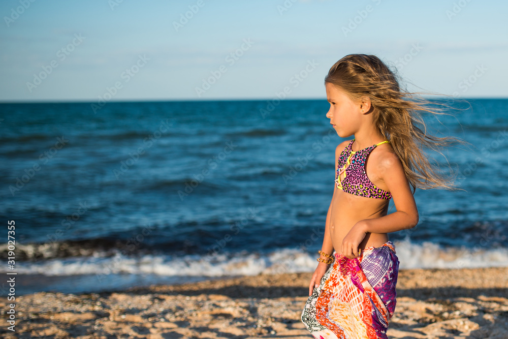 Beautiful relaxed woman resting on the beach by the sea with a scarf on a sunny warm summer day. The concept of the long-awaited vacation and recovery. Copyspace