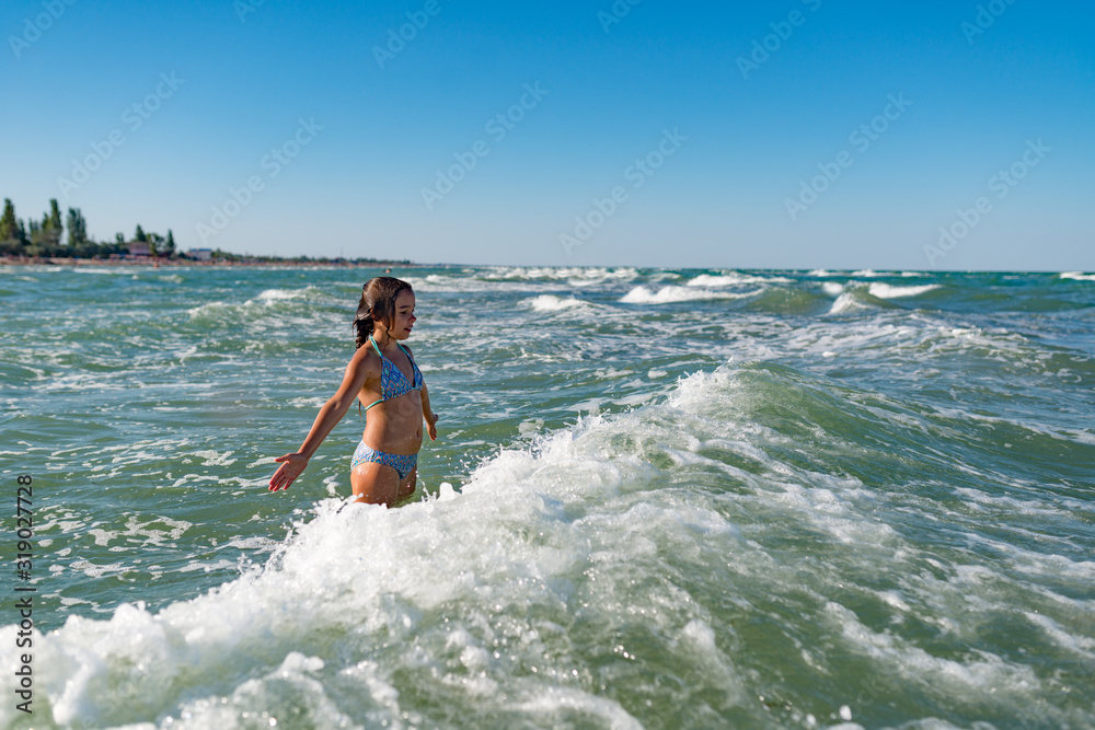 Little funny active happy girl splashing in the noisy sea waves on a sunny warm summer day. Sea vacation concept with kids. Advertising space Little funny active happy girl splashing in the noisy sea waves on a sunny warm summer day. Sea vacation concept with kids. Advertising space