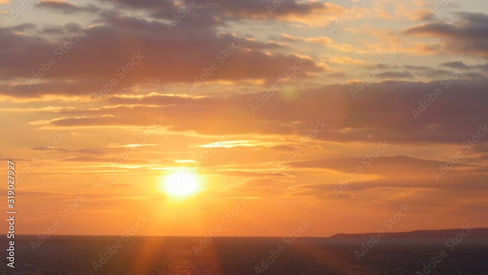 beautiful sunset on the background of sea, sun going beyond the horizon illuminating water and clouds in the sky