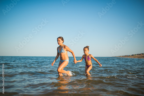 Two happy and positive girls sisters run along the sea waves during their vacation on a sunny hot summer day. Family vacation concept abroad. Copyspace