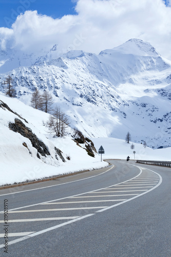 Asphalt road in an alpine valley with mountain peaks covered with fresh snow .