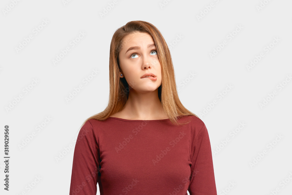 Portrait girl confused frightened look bite lip. Beautiful young woman wears Burgundy-colored jacket sleeves isolated on white background in Studio with an empty space for text and advertising. Portrait girl confused frightened look bite lip. Beautiful young woman wears Burgundy-colored jacket sleeves isolated on white background in Studio with an empty space for text and advertising.