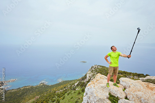 A tourist at the top of a mountain takes a selfie on an action camera.