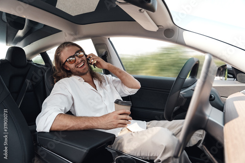 Young adult man sitting in car, talking on smartphone © Viktoriia