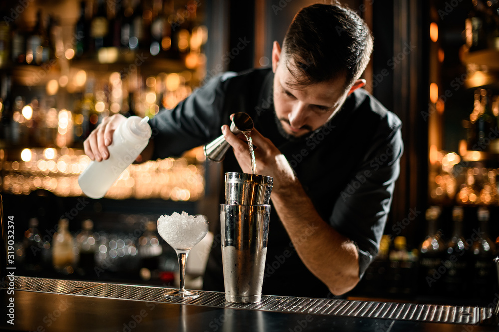 Male bartender precisely flows alcohol from jigger to glass