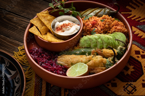 Vegetarian Mexican bowl containing rice, stuffed chilies, beet side, avocado, sour cream and pickles