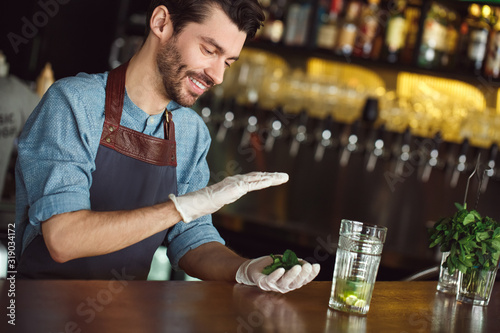 Making Drink. Bartender standing at counter holding mint leaves smiling cheerful photo