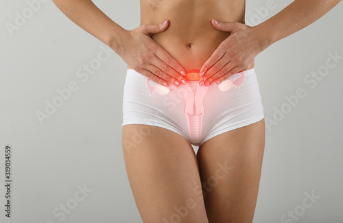 Young woman with drawing of reproductive system on light background. Gynecology concept photo