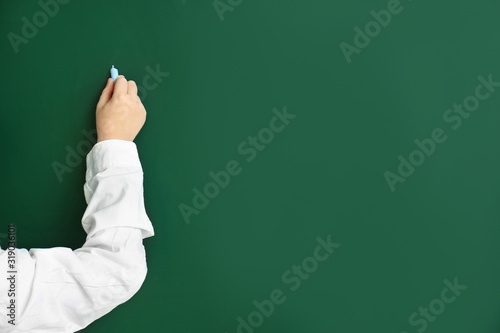Little schoolboy writing on blackboard in classroom