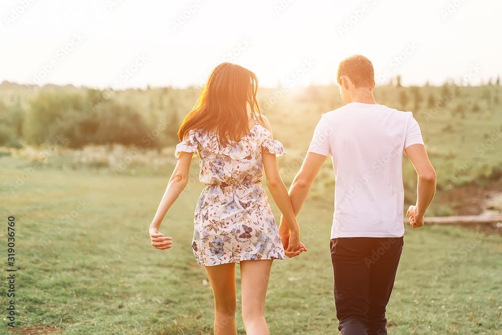 Young couple in love run on through grass field. Walking along grass field.