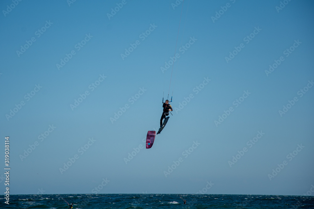 a man flying after doing a kitesurf trick in the air, with more kite surfers in the scene. a man flying after doing a kitesurf trick in the air, with more kite surfers in the scene.