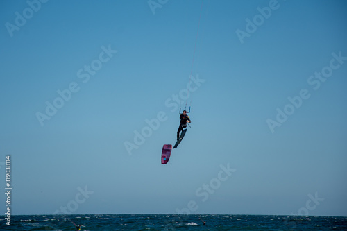 a man flying after doing a kitesurf trick in the air, with more kite surfers in the scene.